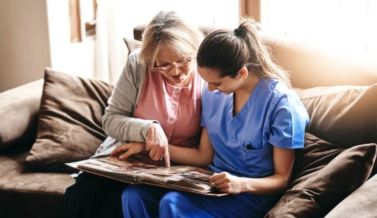 caregiver and older female patient sitting on couch and reading