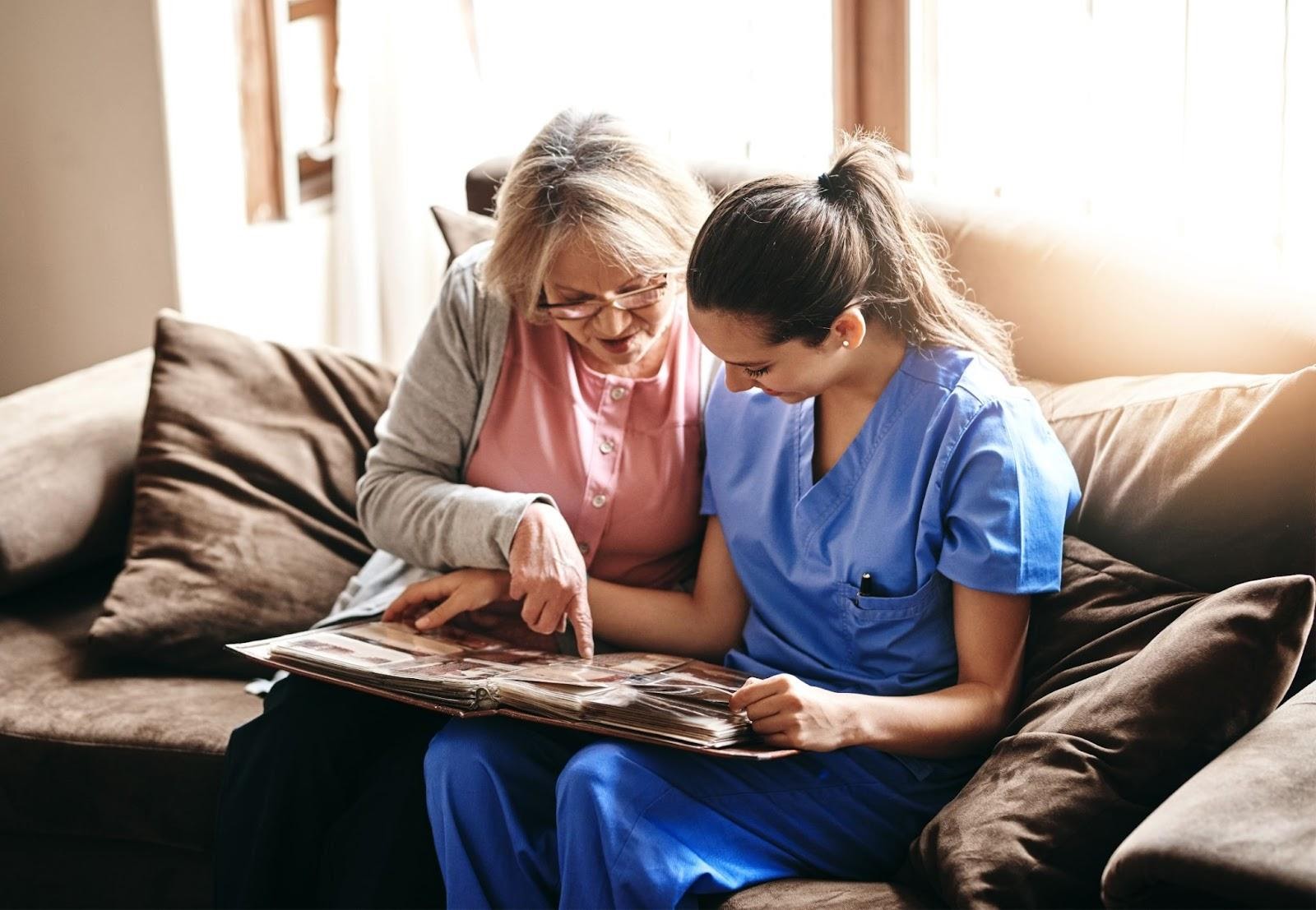 caregiver and older female patient sitting on couch and reading