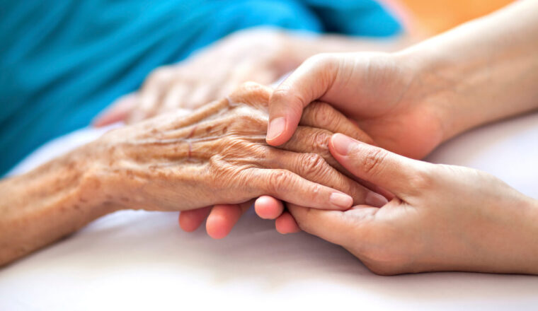 Woman holding senior woman's hand on bed